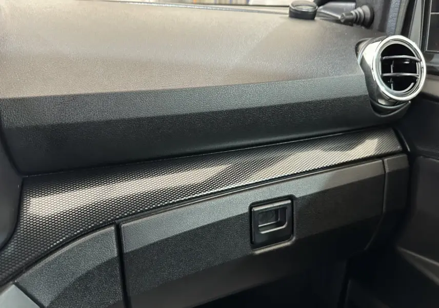 Détail de la planche de bord noire avec insert texturé et sortie d'air ronde côté passager d'une Aixam Ambition rouge.