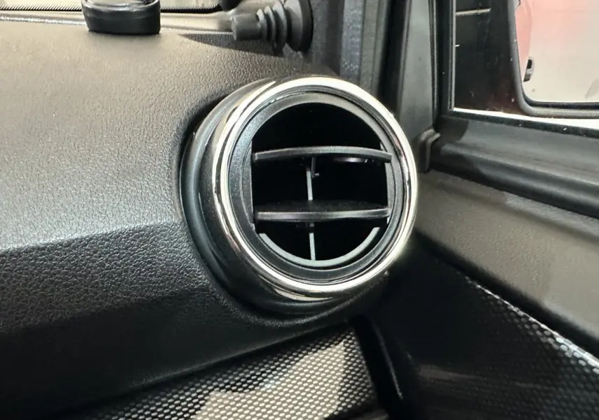 Détail de la sortie d'air ronde chromée côté conducteur dans l'habitacle d'une Aixam Ambition rouge 2025.