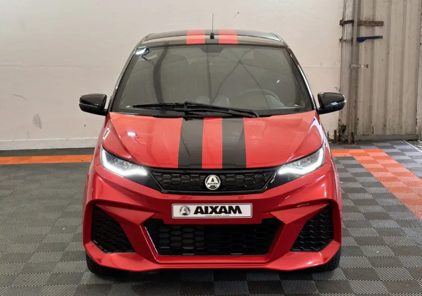 Vue frontale d'une Aixam Ambition 0.5 City Coupe GTI rouge avec bandes noires et rétroviseurs noirs dans un garage.