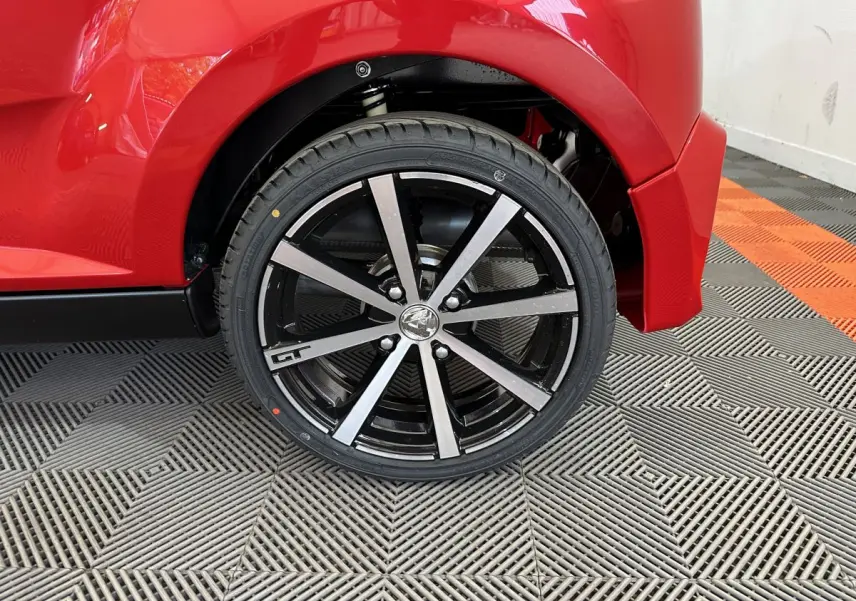 Gros plan sur la roue arrière droite rouge de l'AIXAM AMBITION 0.5 CITY COUPE GTI avec jante noire et argentée marquée GT