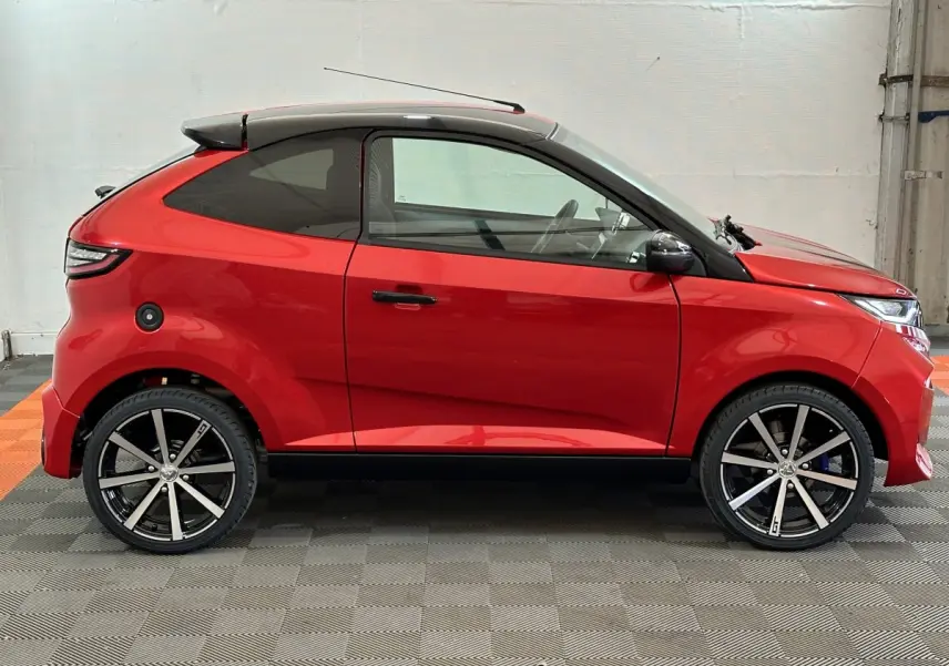 Vue latérale gauche d'une Aixam Ambition 0.5 City Coupe GTI rouge avec toit noir et jantes alliage modernes.