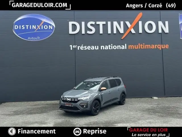 Vue 3/4 avant d'une Dacia Jogger Extreme+ Hybrid 140 2025 gris clair avec jantes noires devant un mur gris.