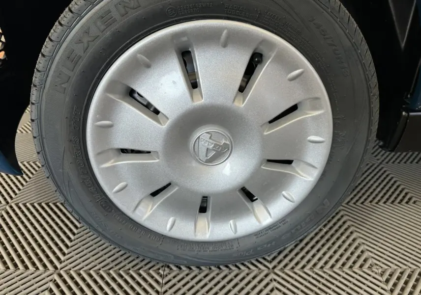 Gros plan sur la roue avant droite d'une Aixam Ambition bleu 2025 avec enjoliveur gris et logo central marqué.