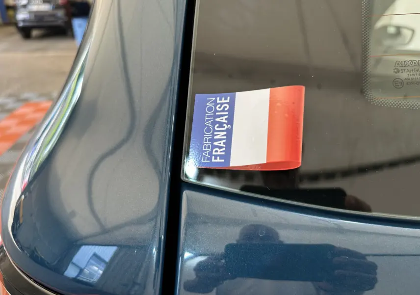 Gros plan sur la partie arrière gauche bleu métallisé d'une Aixam Ambition 0.5 City Pack avec autocollant "Fabrication Française" visible.