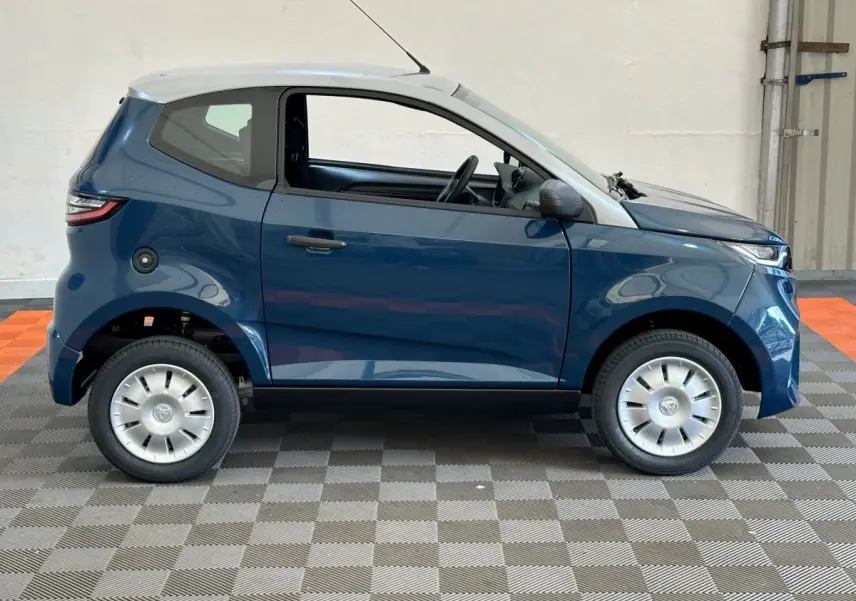 Profil côté droit de l'AIXAM AMBITION 0.5 CITY PACK 2025 bleu avec toit blanc et rétroviseur caméra côté conducteur.