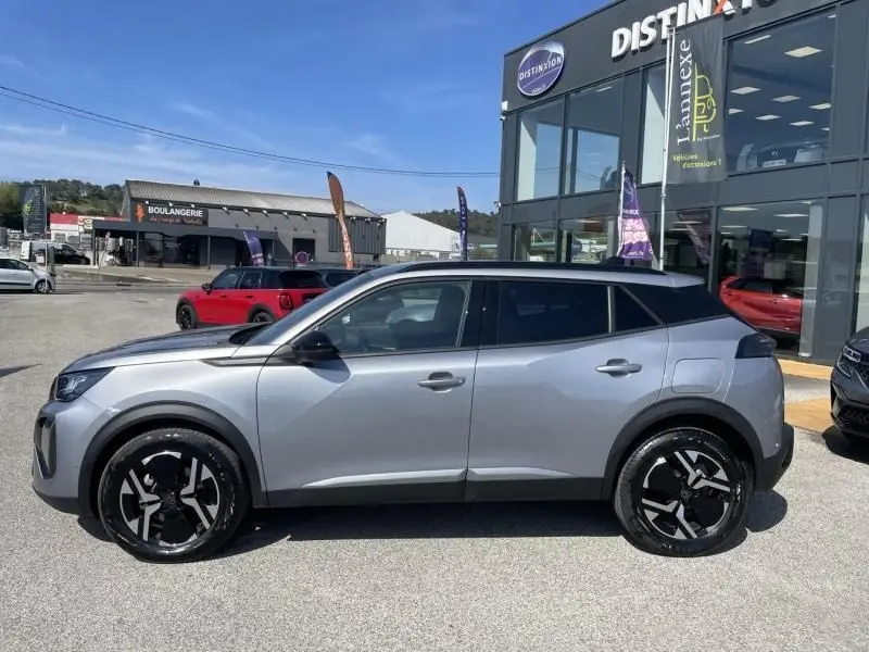 Vue de profil côté gauche d'un Peugeot 2008 gris métal 2025 avec jantes noires distinctives, stationné devant un concessionnaire.