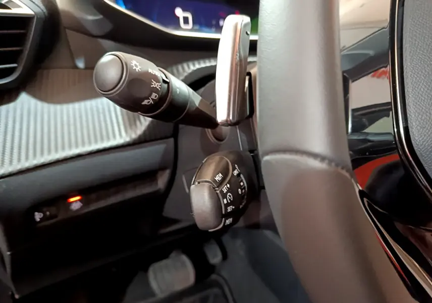 Gros plan intérieur sur la colonne de direction et commandes au volant cuir noir de la Peugeot 208 gris foncé.
