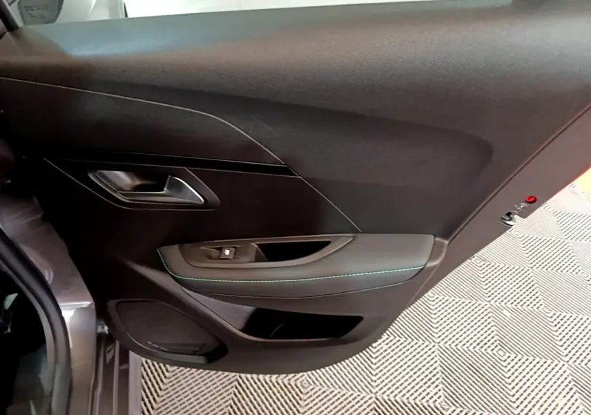 Vue intérieure du panneau de porte côté gauche de la Peugeot 208 gris foncé avec surpiqûres bleues et commande de fenêtre.