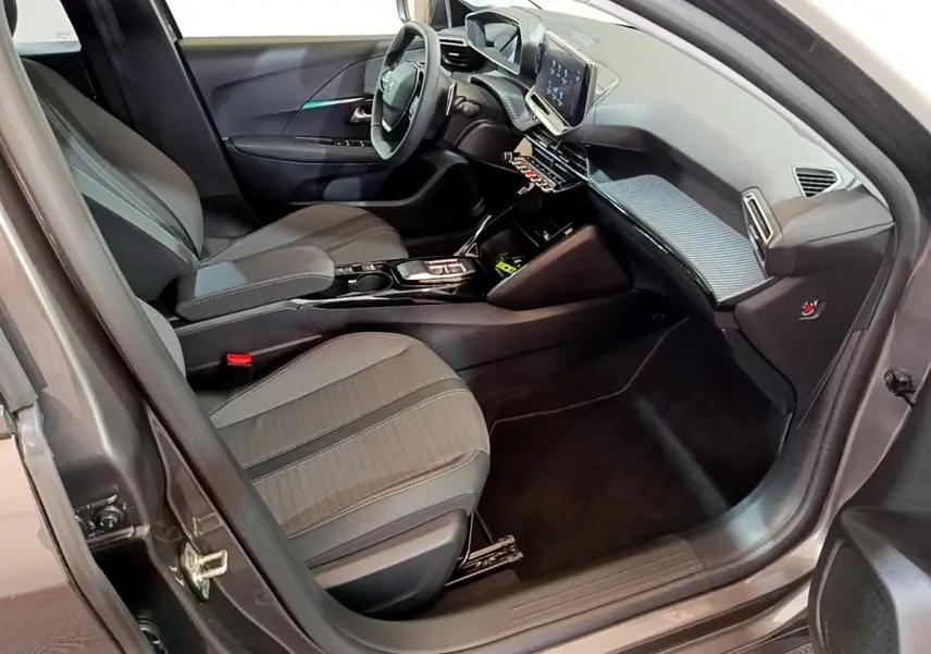 Vue intérieure côté conducteur de la Peugeot 208 gris foncé 2022, avec tableau de bord digital et sièges tissu noirs.