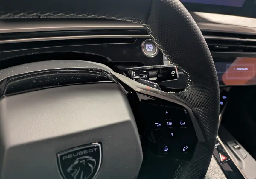 Vue rapprochée du volant cuir perforé noir du Peugeot 3008 Hybrid 145 GT avec commandes tactiles et bouton start/stop.