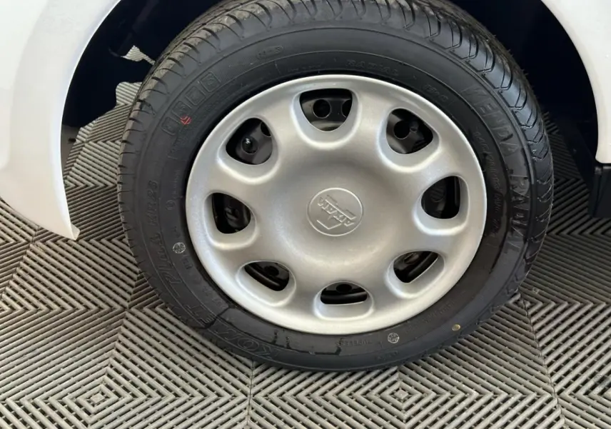 Gros plan sur la roue arrière droite d'une Aixam Minauto E Access blanche de 2025, avec pneu noir sur sol texturé.