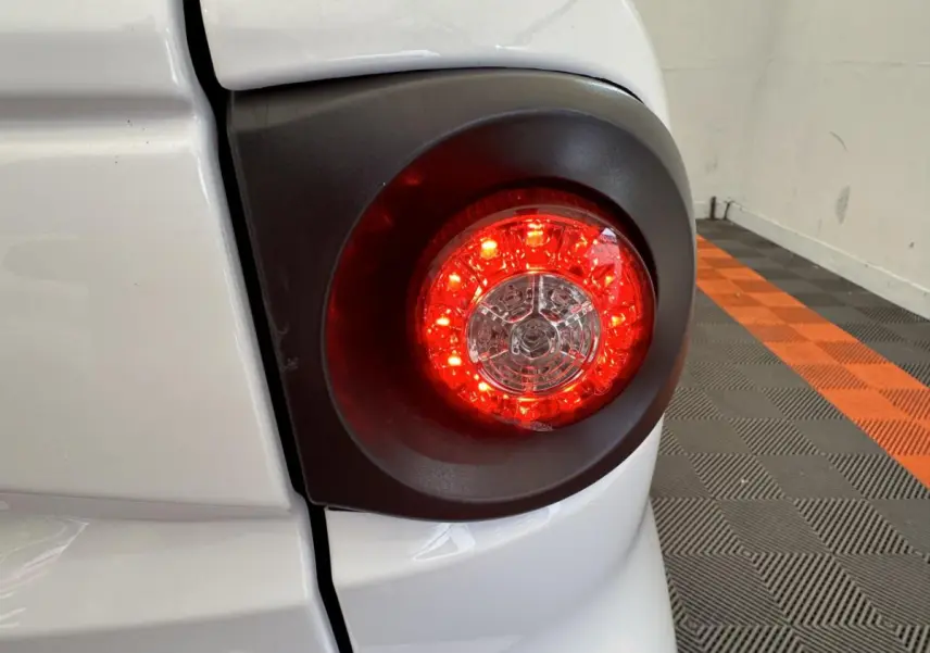 Gros plan sur le feu arrière droit rouge du véhicule blanc Aixam MINAUTO E ACCESS 2025 dans un garage.