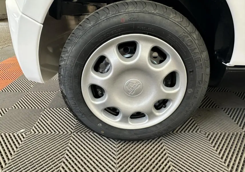 Gros plan sur la roue arrière droite blanche d'une Aixam Minauto E Access 2025 électrique sur sol texturé.