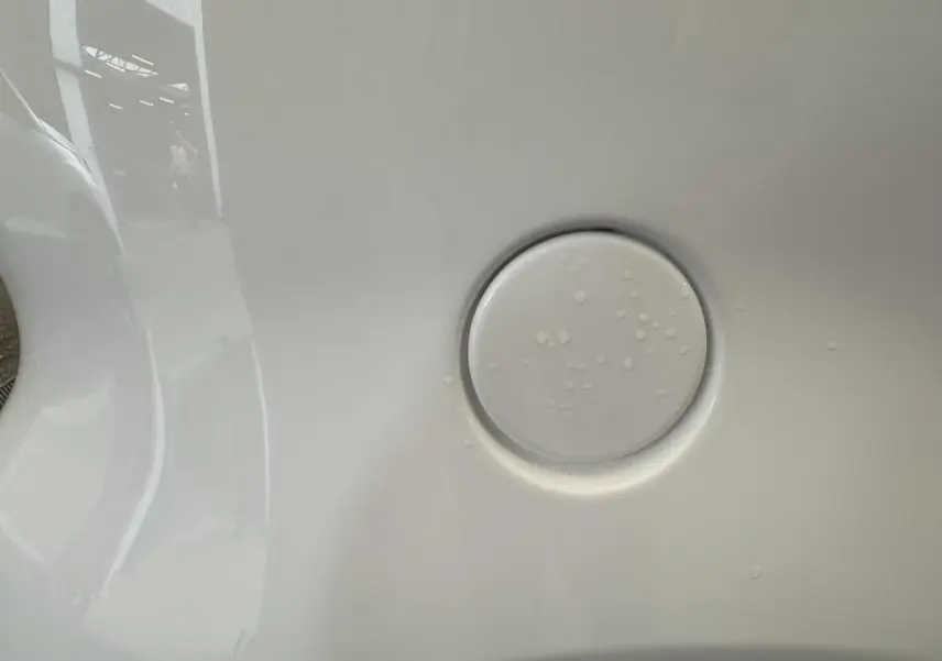 Gros plan sur la trappe de recharge blanche de l'AIXAM MINAUTO E ACCESS 2025 côté conducteur avec reflets et gouttes d'eau.