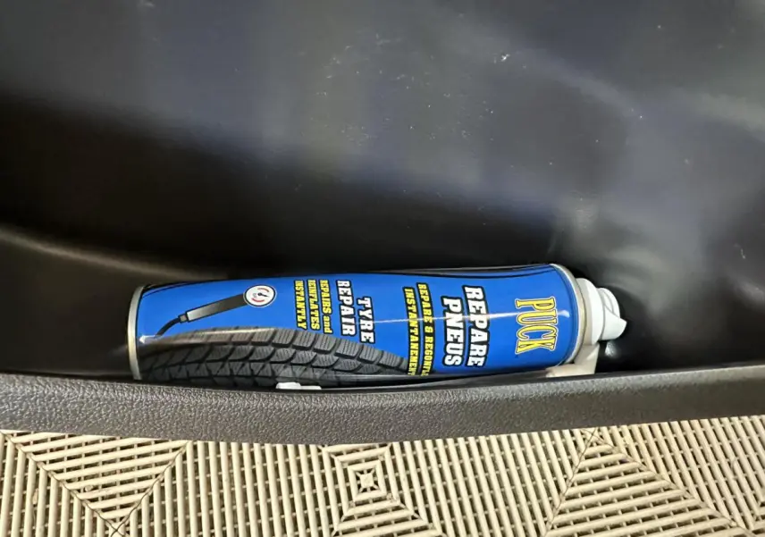 Gros plan sur une bombe de réparation de pneus bleue dans le rangement côté conducteur d'une Aixam Minauto E Access blanche.