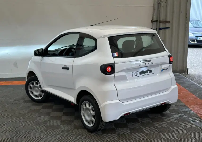 Vue 3/4 arrière droite d'une Aixam Minauto E Access blanche avec feux ronds et caméra sur le rétroviseur côté conducteur.