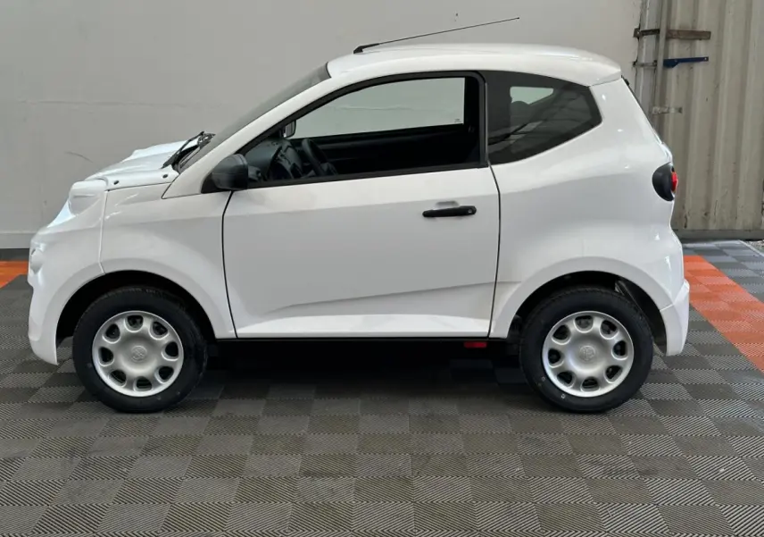 Vue de profil côté gauche d'une Aixam Minauto E Access blanche électrique avec rétroviseur caméra conducteur visible.
