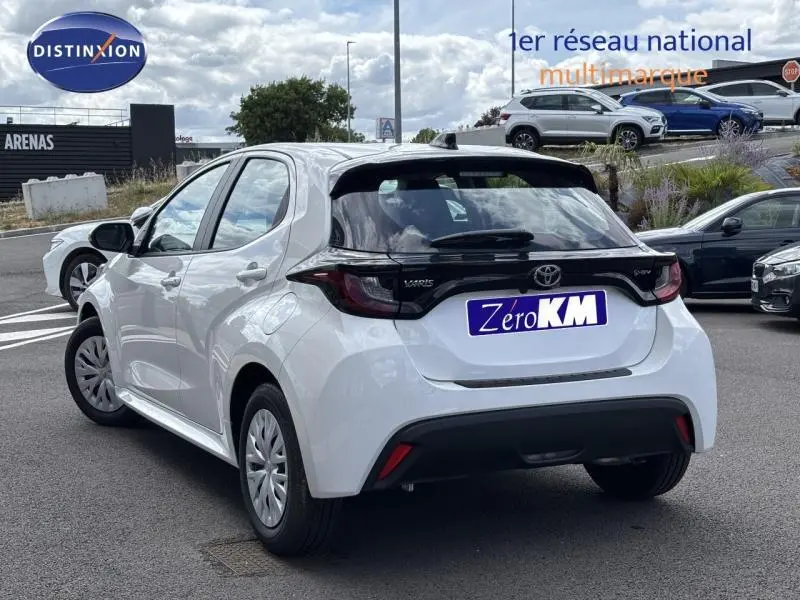 Toyota Yaris 116h Dynamic blanc vue 3/4 arrière droit avec feux arrière noirs et jantes acier.
