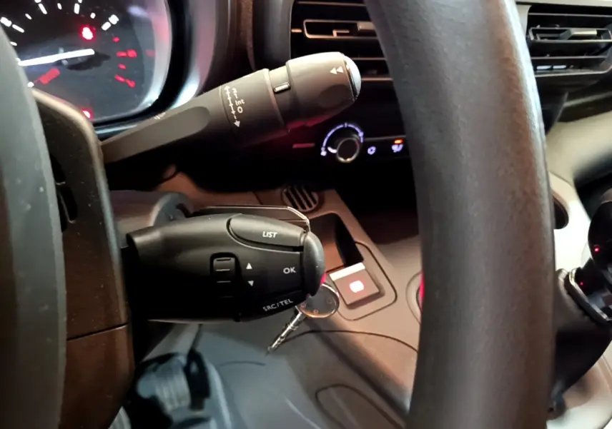 Gros plan sur le volant et commandes au volant du Citroën Berlingo blanc, avec tableau de bord et clés visibles.