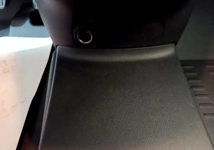 Gros plan sur la console centrale noire du Citroën Berlingo blanc, montrant une prise 12V et un tapis de sol.