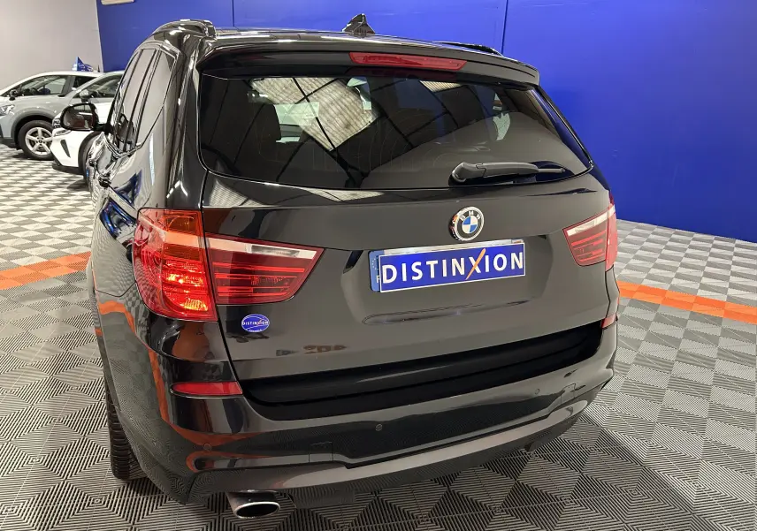Vue 3/4 arrière d’un BMW X3 noir avec attelage, feu arrière allumé, dans un showroom au sol à damier.