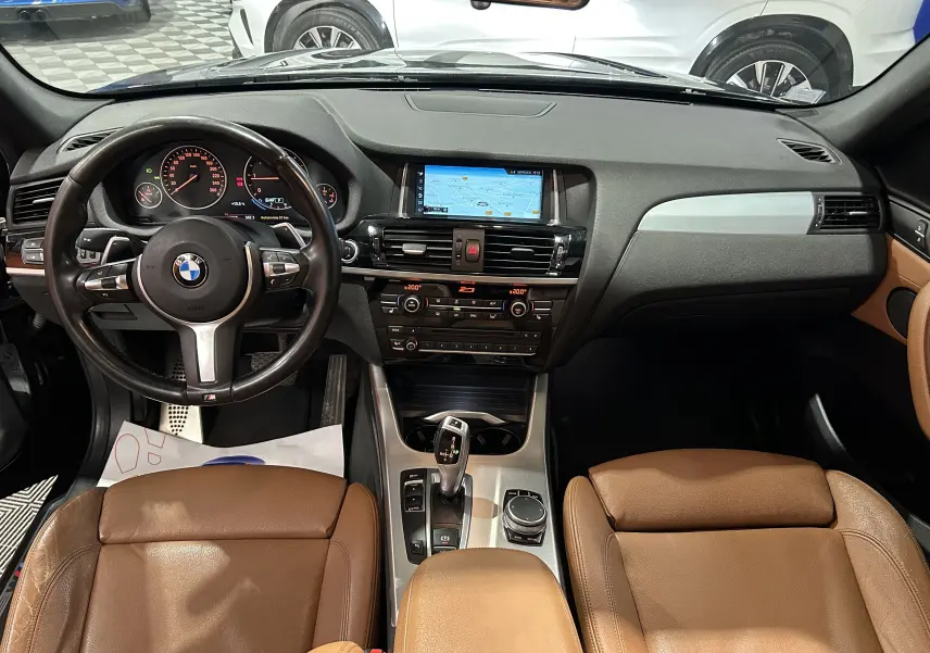 Vue intérieure avant du BMW X3 sDrive18dA 2017, avec sièges cuir marron et tableau de bord noir intégrant un écran GPS.