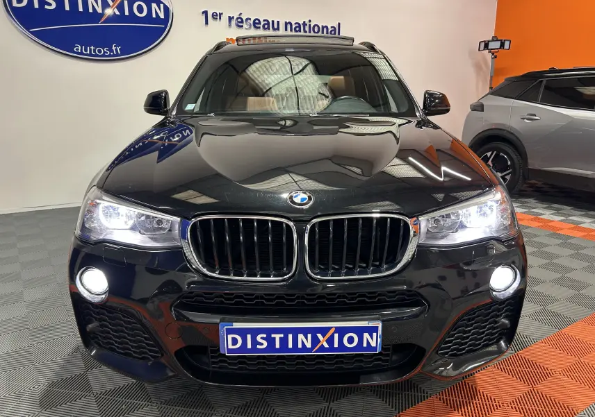 Vue de face d'un BMW X3 noir avec phares et feux antibrouillard allumés, dans un showroom intérieur.