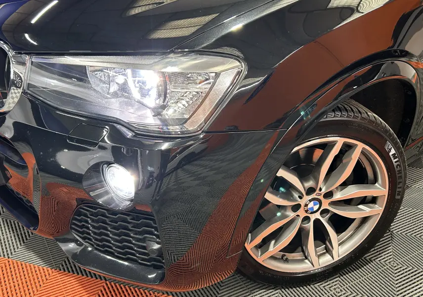Gros plan sur l'avant droit noir brillant d'une BMW X3 2017 avec phare et jante alliage visible.