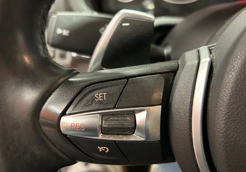 Gros plan sur les commandes de régulateur de vitesse sur le volant cuir noir du BMW X3 sDrive18dA 2017.