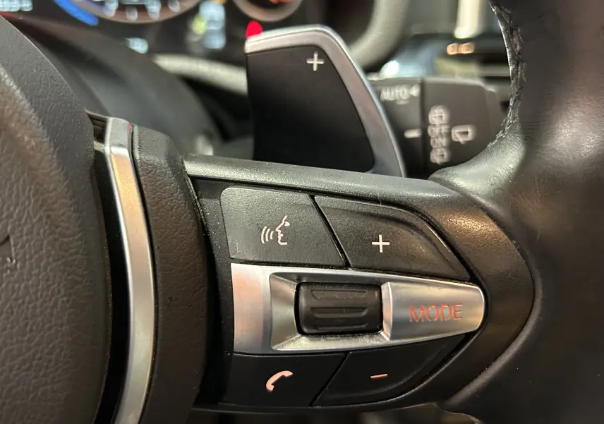 Gros plan sur les commandes multifonctions noires et argentées du volant du BMW X3 noir, avec bouton mode en rouge.