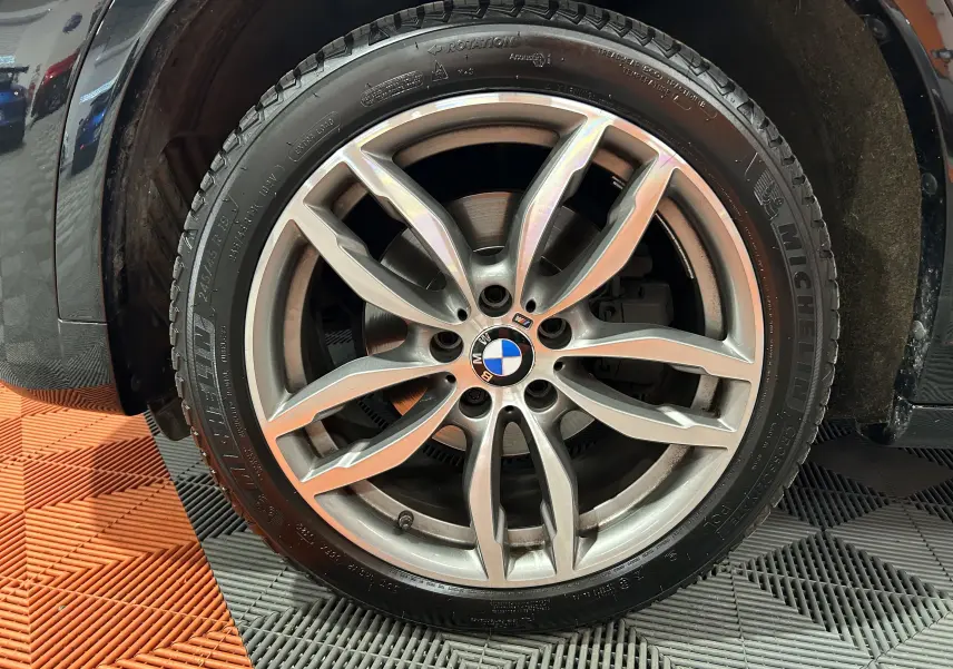 Gros plan sur la roue avant gauche d’un BMW X3 noir, mettant en valeur la jante en alliage à design sportif et le pneu Michelin.