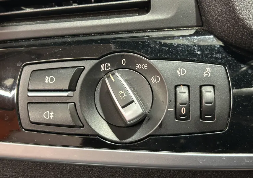 Gros plan sur le panneau de commande des phares noir brillant à l'intérieur d'une BMW X3 noire de 2017.