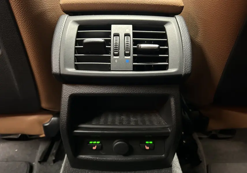 Vue rapprochée de la console arrière avec aérateurs et commandes de sièges chauffants sur BMW X3 noir, intérieur cuir marron.
