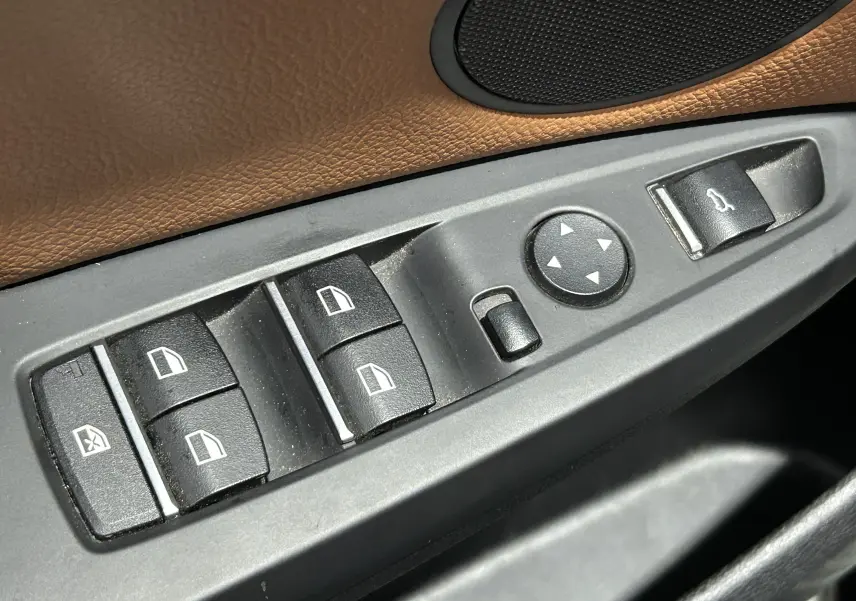 Gros plan sur les commandes de lève-vitres et rétroviseurs côté conducteur avec garniture cuir marron d’un BMW X3 noir.