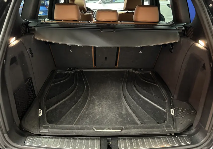 Coffre ouvert vu de l'arrière d'un BMW X3 noir avec tapis de coffre BMW et sièges arrière en cuir marron.