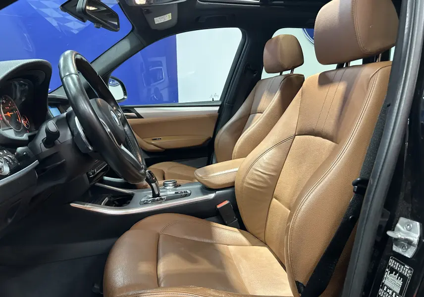 Vue intérieure côté conducteur d'une BMW X3 2017 avec sièges en cuir marron et volant multifonction noir.