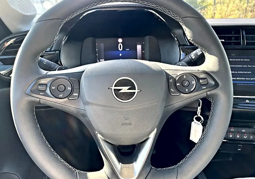 Vue rapprochée du volant sport noir avec surpiqûres blanches de l'Opel Corsa 2025, tableau de bord et écran tactile en arrière-plan.