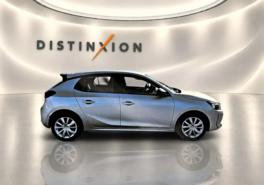 Opel Corsa gris alu vue de profil côté gauche dans un showroom avec reflet au sol et logo Distinxion en arrière-plan.