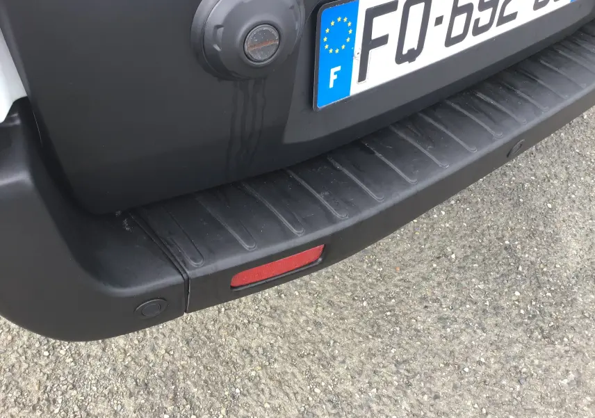 Gros plan sur le pare-chocs arrière noir du Ford Transit blanc avec plaque d'immatriculation française visible.
