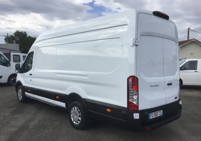 Vue 3/4 arrière droite d'un fourgon Ford Transit blanc avec toit surélevé et feux arrière verticaux.