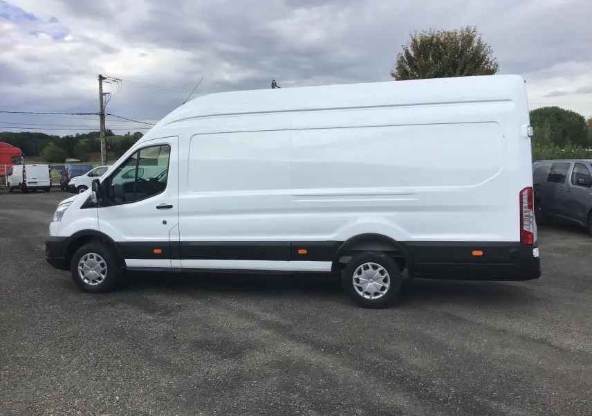 Vue latérale gauche d'un fourgon Ford Transit blanc à toit élevé avec protections noires et feux arrière verticaux.
