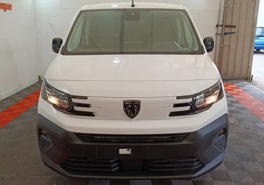 Vue frontale d'un Peugeot Partner XL blanc avec calandre noire et phares allumés en intérieur.