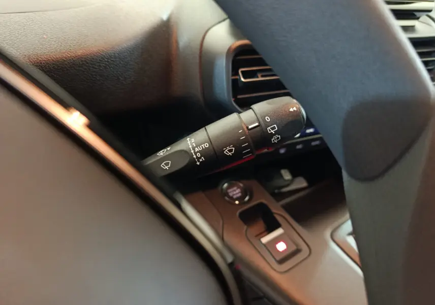 Gros plan sur la manette d'essuie-glace à gauche du volant dans l'habitacle sombre du Peugeot Partner blanc 2025.