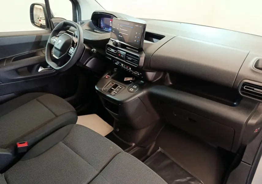 Intérieur du Peugeot Partner XL 2025 vu côté passager, tableau de bord noir avec écran tactile central et sièges gris foncé.