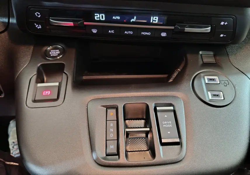 Vue rapprochée de la console centrale noire du Peugeot Partner 2025 avec commandes de climatisation et boîte automatique.