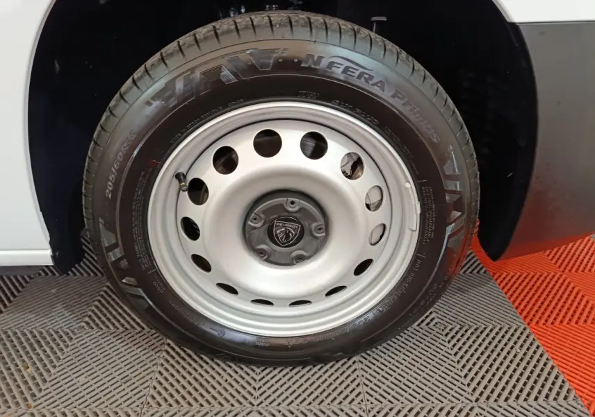 Gros plan sur la roue avant droite d'un Peugeot Partner blanc avec jante acier et logo Peugeot central.