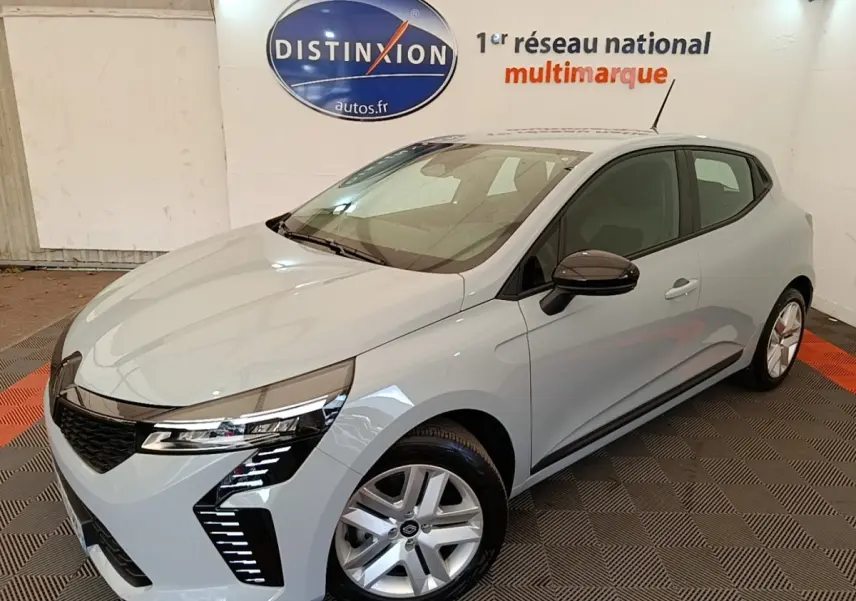 Renault Clio gris clair vue 3/4 avant droit en intérieur avec feux LED et jantes alliage visibles.