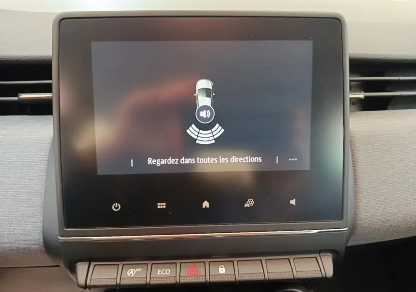 Écran tactile central de la Renault Clio gris clair affichant l'alerte de détection d'obstacles avec message "Regardez dans toutes les directions".