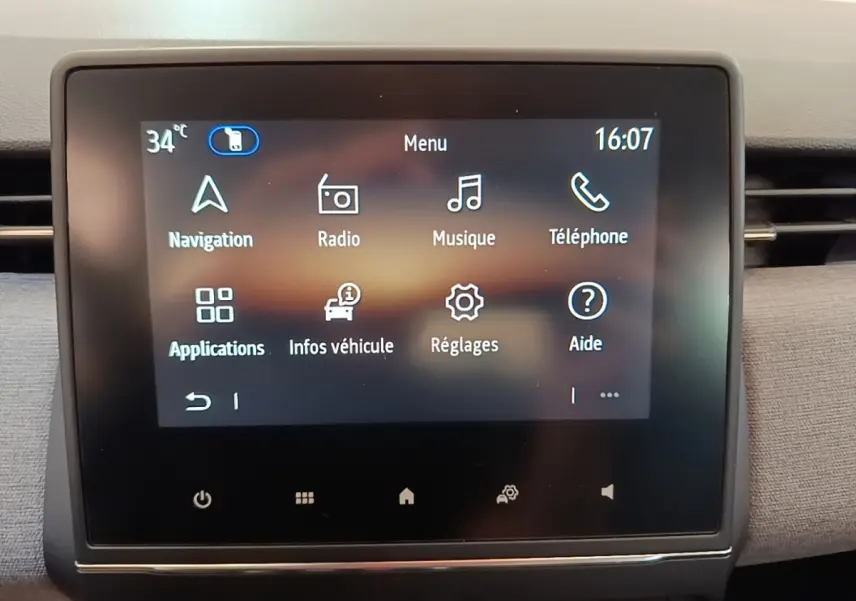 Écran tactile central du tableau de bord de la Renault Clio gris clair, affichant le menu principal avec navigation et radio.