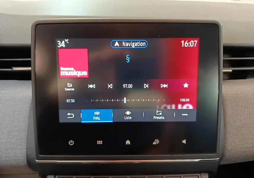 Écran tactile central de la Renault Clio gris clair, affichant la radio et la navigation, vue intérieure frontale.